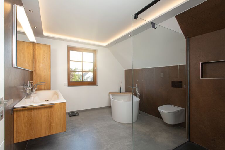 Blick in ein hochmodernes Bad mit Dusch-WC, freistehender Badewanne, bodenebener Dusche und Waschtischlösung in Holzoptik