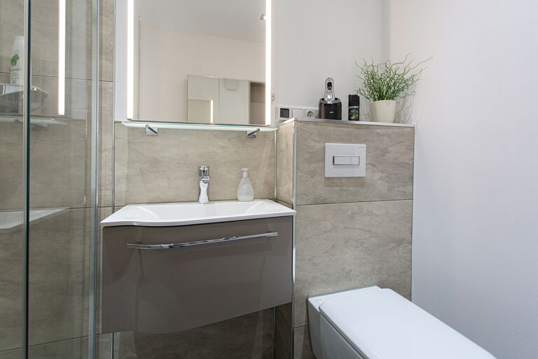 Raumwunder: Blick in ein modern umgebautes Neubau-Bad ohne Fenster mit moderner WC- und Waschtischanlage und komfortabler Dusche mit Glastrennwand
